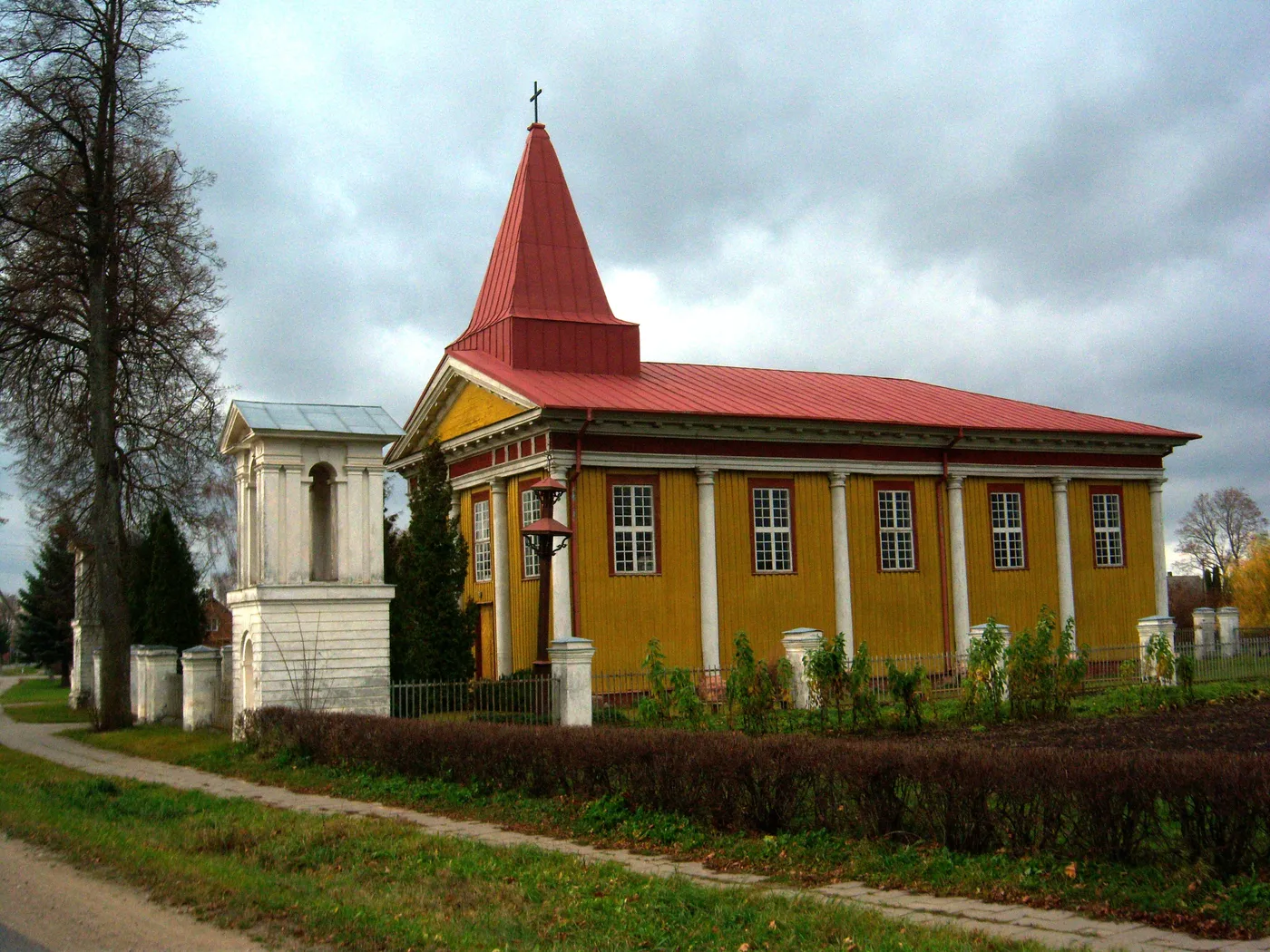 Medinė geltona Raguvėlės bažnyčia raudonu stogu ir balta varpinė